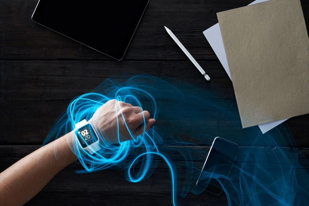 A man's hand wearing a smartwatch, interacting with connected portable devices.