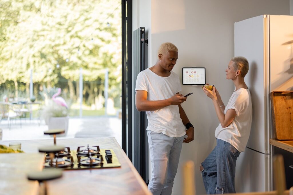 Couple standing by a smart home thermostat as they talk about setting the perfect temperature.