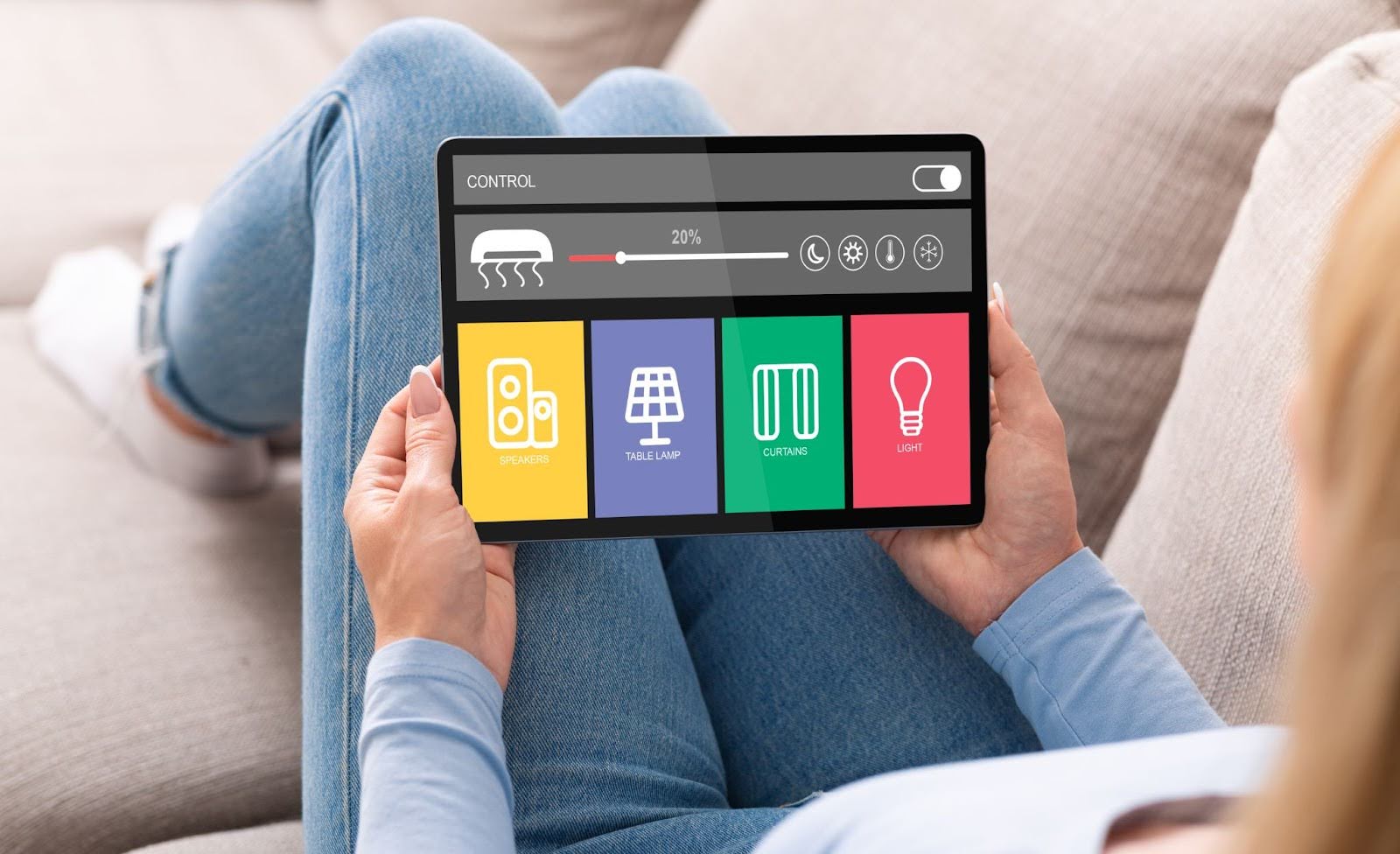 Rear view of a homemaker using a tablet to control smart home features like lighting, climate, sound, ventilation, and energy usage.