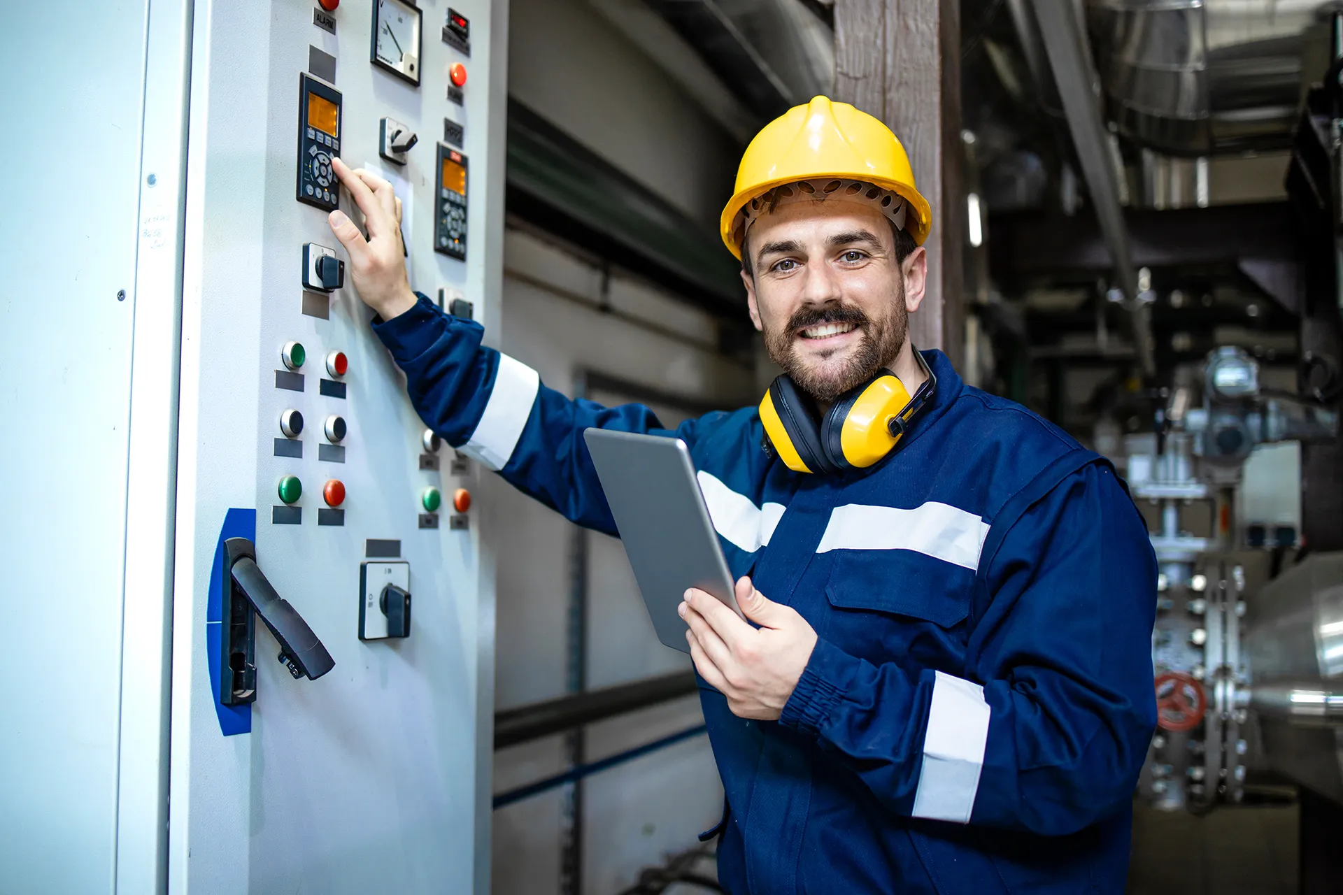 Male technician in a white hard hat and safety vest, connecting wires in a server room or electrical panel