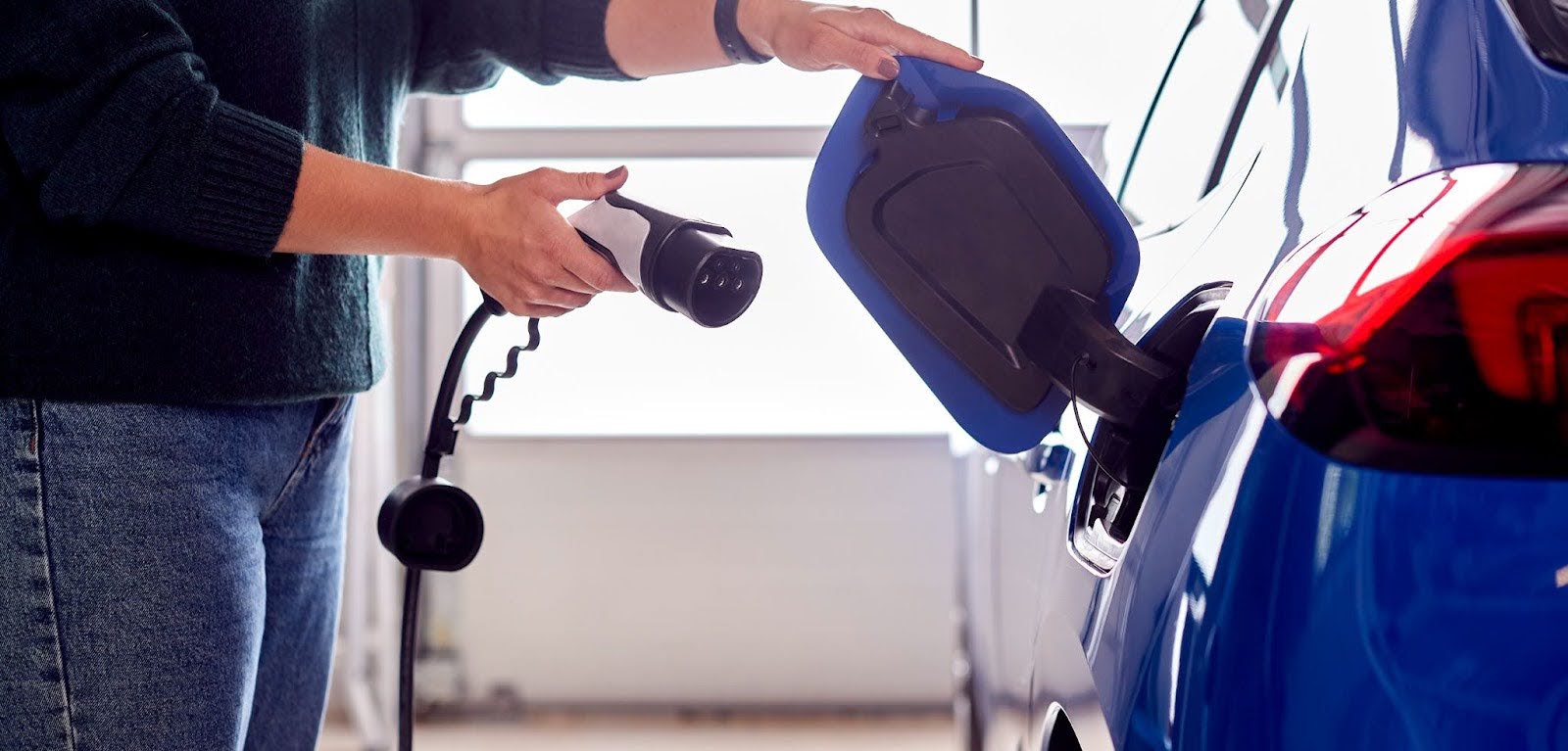 Close up on a hand attaching a charging cable to an electric car.