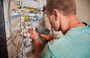 Electrician repairing a home service panel using a power drill.