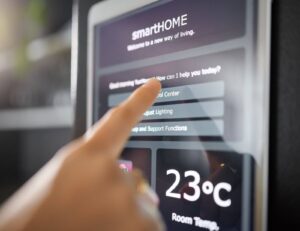 Woman’s hand adjusting smart home thermostat on a wall using a digital app display.