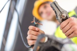 Electrician cutting residential electrical wiring with wire cutters during a home safety repair.